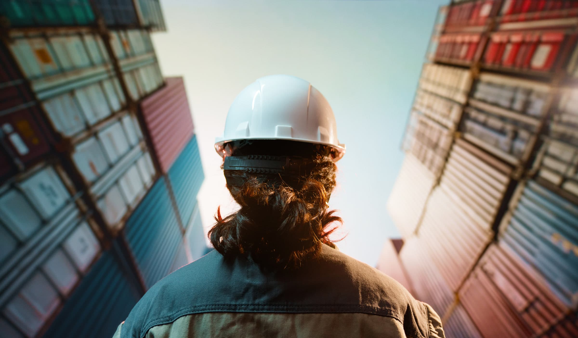Worker in a hard hat looking up at stacked shipping containers
