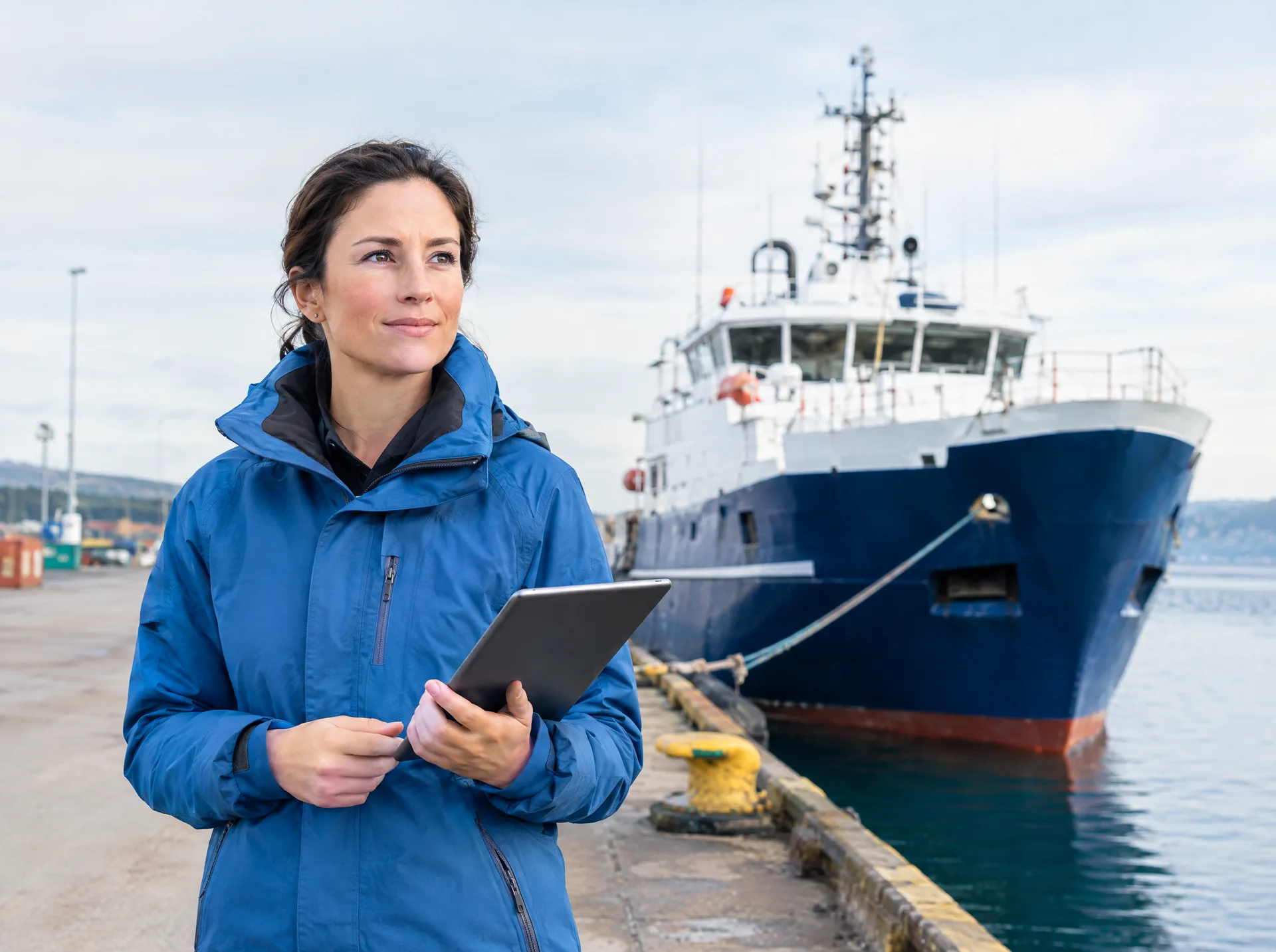 Port officer with a tablet on a quay beside a ship