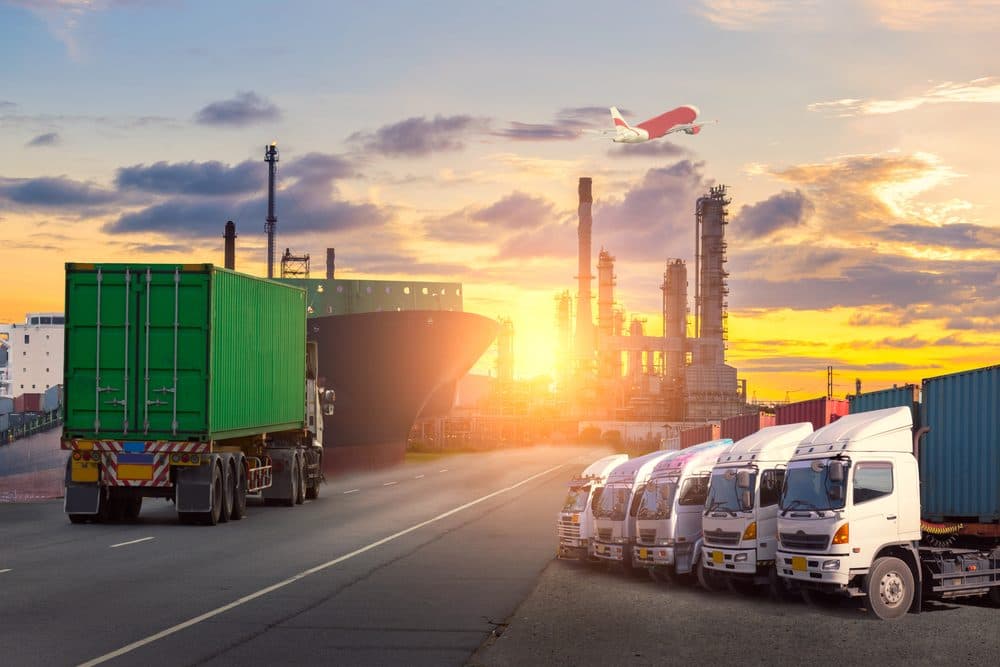 Container ship, trucks and a refinery at sunset with an aircraft overhead