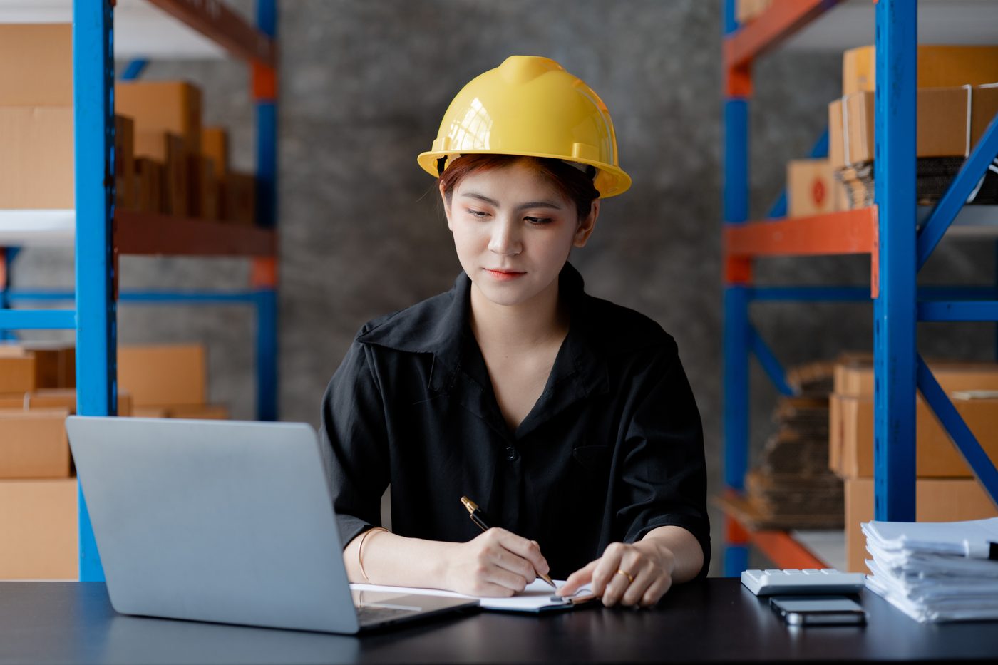 A warehouse supervisor in a hard hat working at a laptop