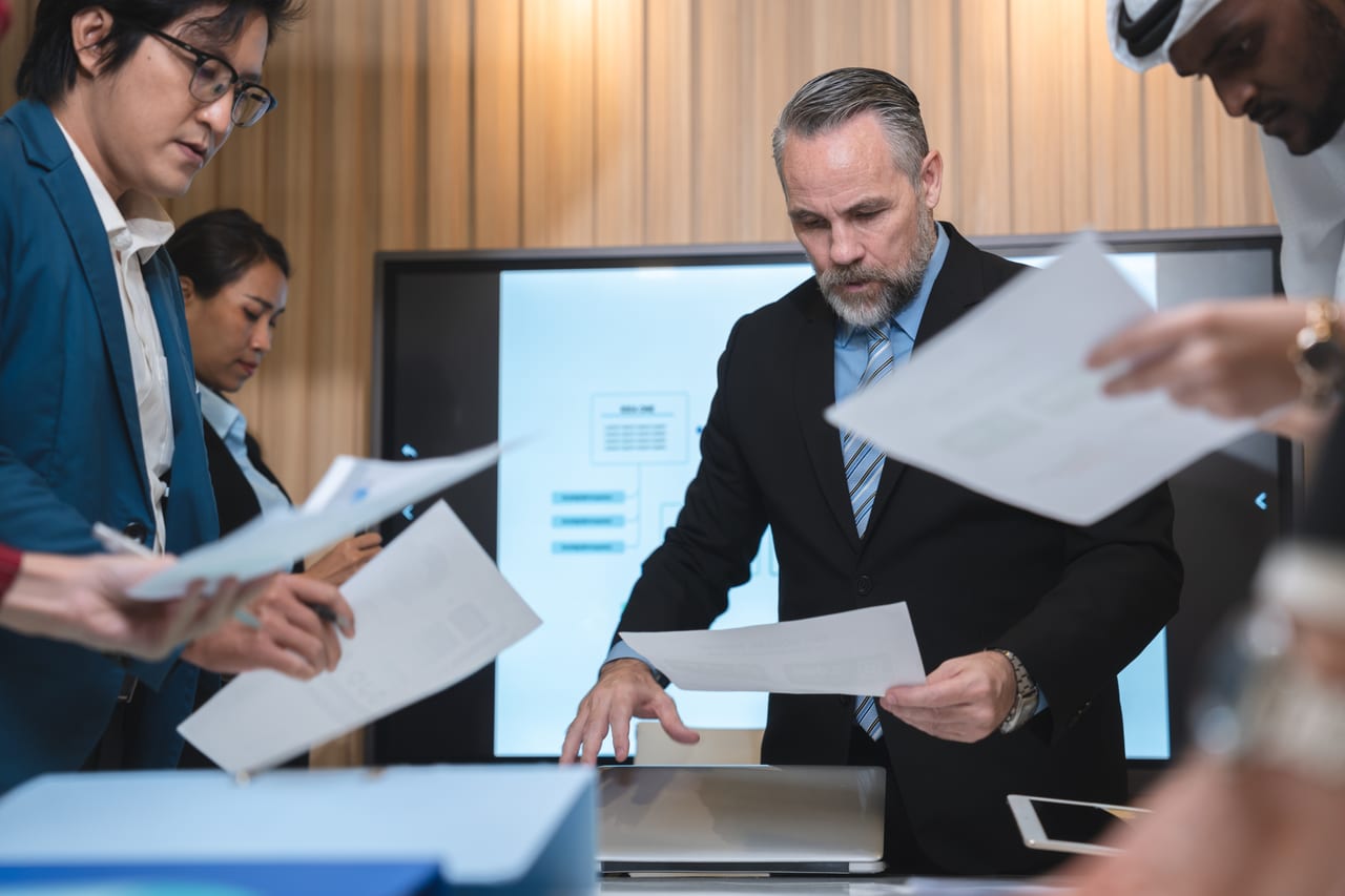 Colleagues reviewing documents around a meeting-room screen