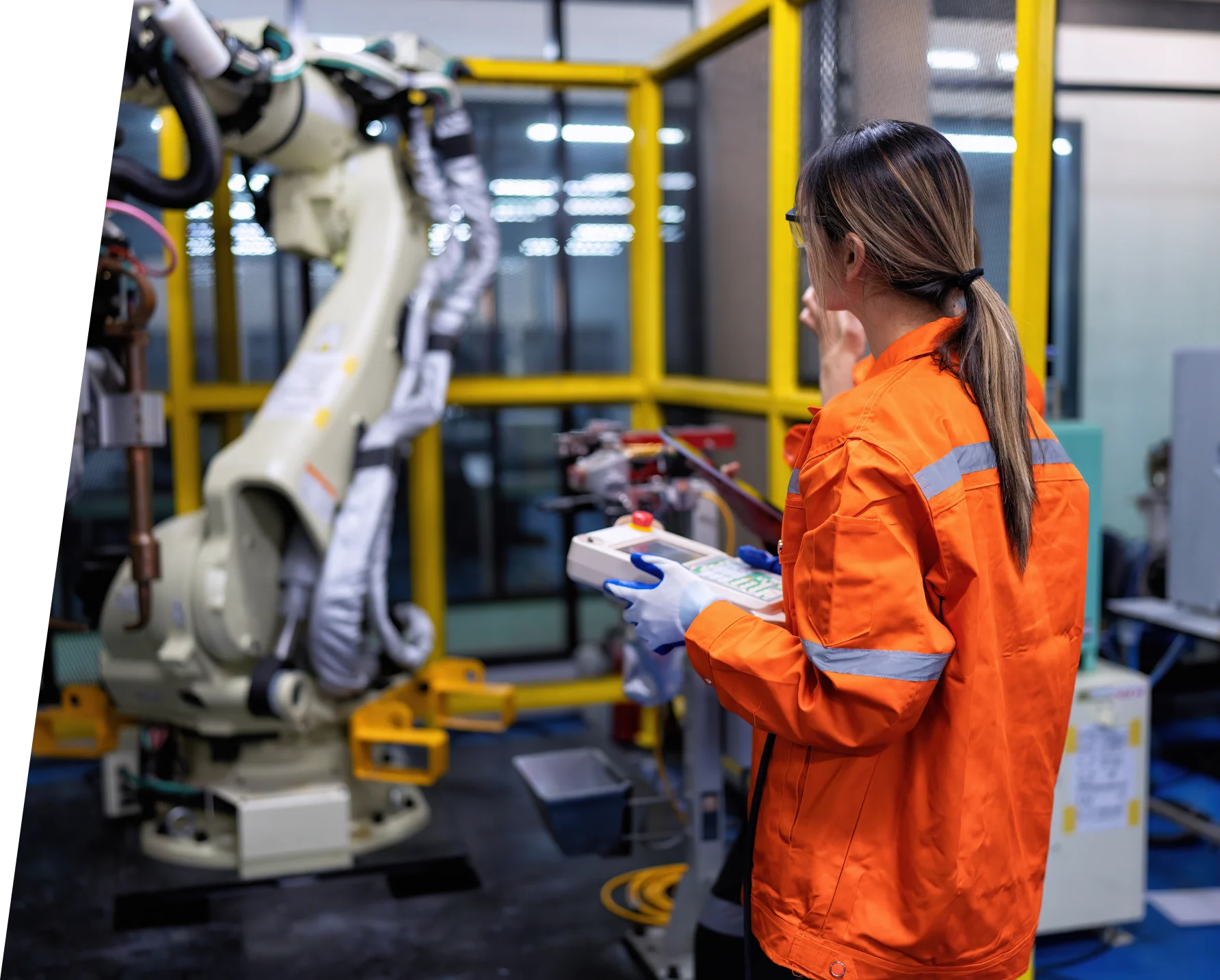 Technician in high-visibility overalls operating a robotic arm on a production line
